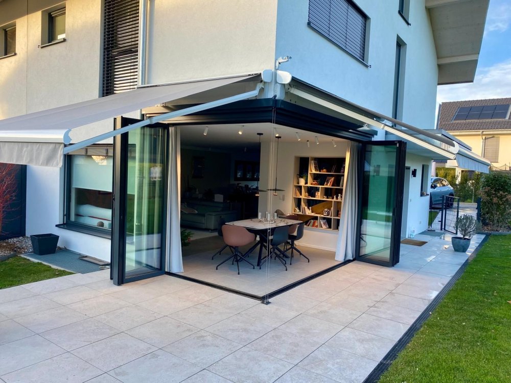 Splendide extension de pièce de vie réalisée grâce à une baie accordéon d’angle, offrant une ouverture maximale sur l’extérieur.